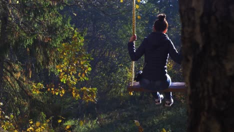 Brunette-girl-swings-in-forest-trail-rope-swing-in-sunny-autumn-day