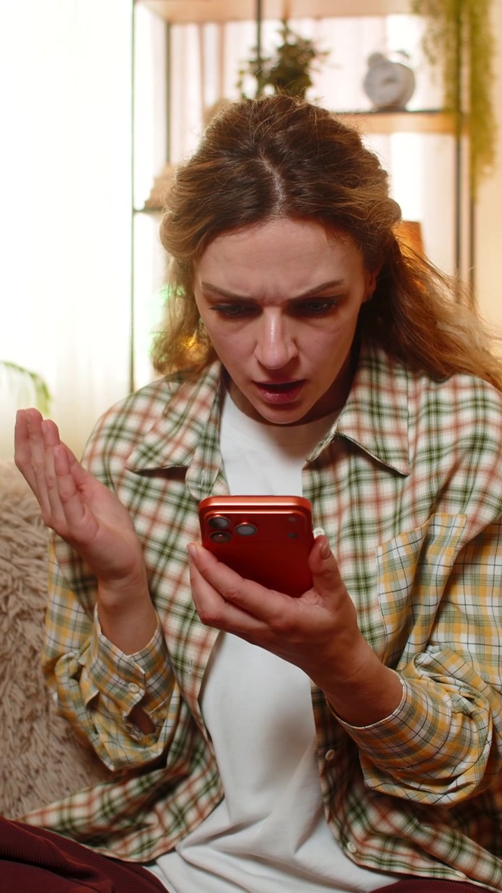 Young woman on home sofa reads order cancellation on smartphone feeling upset after online game loss
