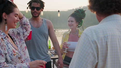 cheerful friends dancing and drinking on lake pier