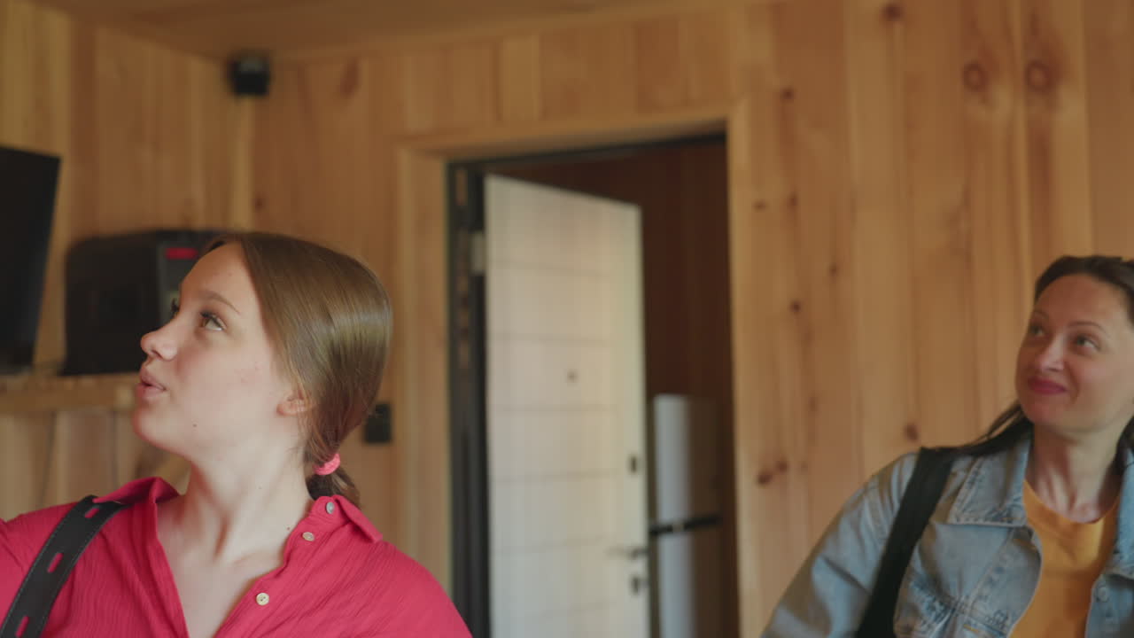 Three friends walk into wooden building with sound system and wall mounted television, looking around with excitement and joy, smiling and exploring cozy wooden interior full of warmth and interest