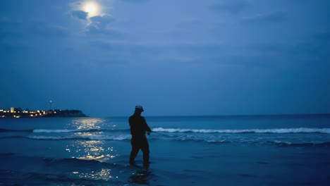 Fisherman-catch-fish-at-night-by-the-beach-standing-on-the-seashore-against-the-moon
