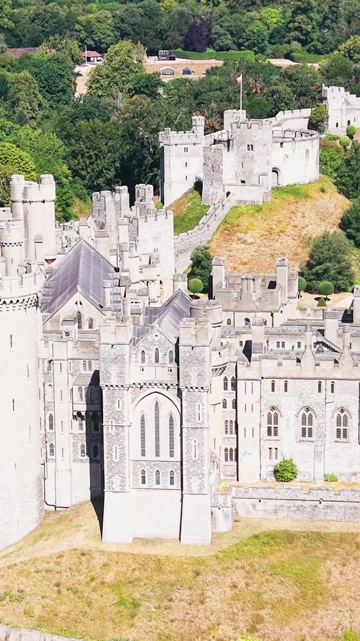 Avvicinamento con drone al Castello di Arundel, con la telecamera fissa sulla fortezza, che si inclina verso il basso mentre si avvicina sopra le cime degli alberi e i giardini paesaggistici nel West Sussex, Inghilterra. Formato verticale per i social media.