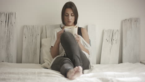 atractiva joven lee un libro en su cama