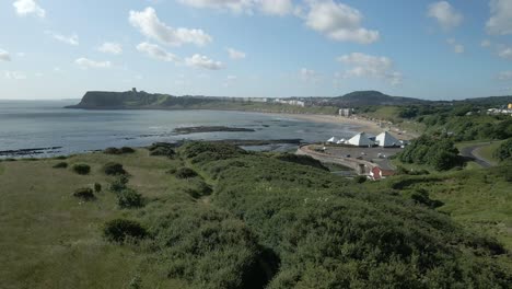 Aerial-view-of-North-bay,-Scarborough,-North-Yorkshire-with-grassland,-ocean,-and-castle