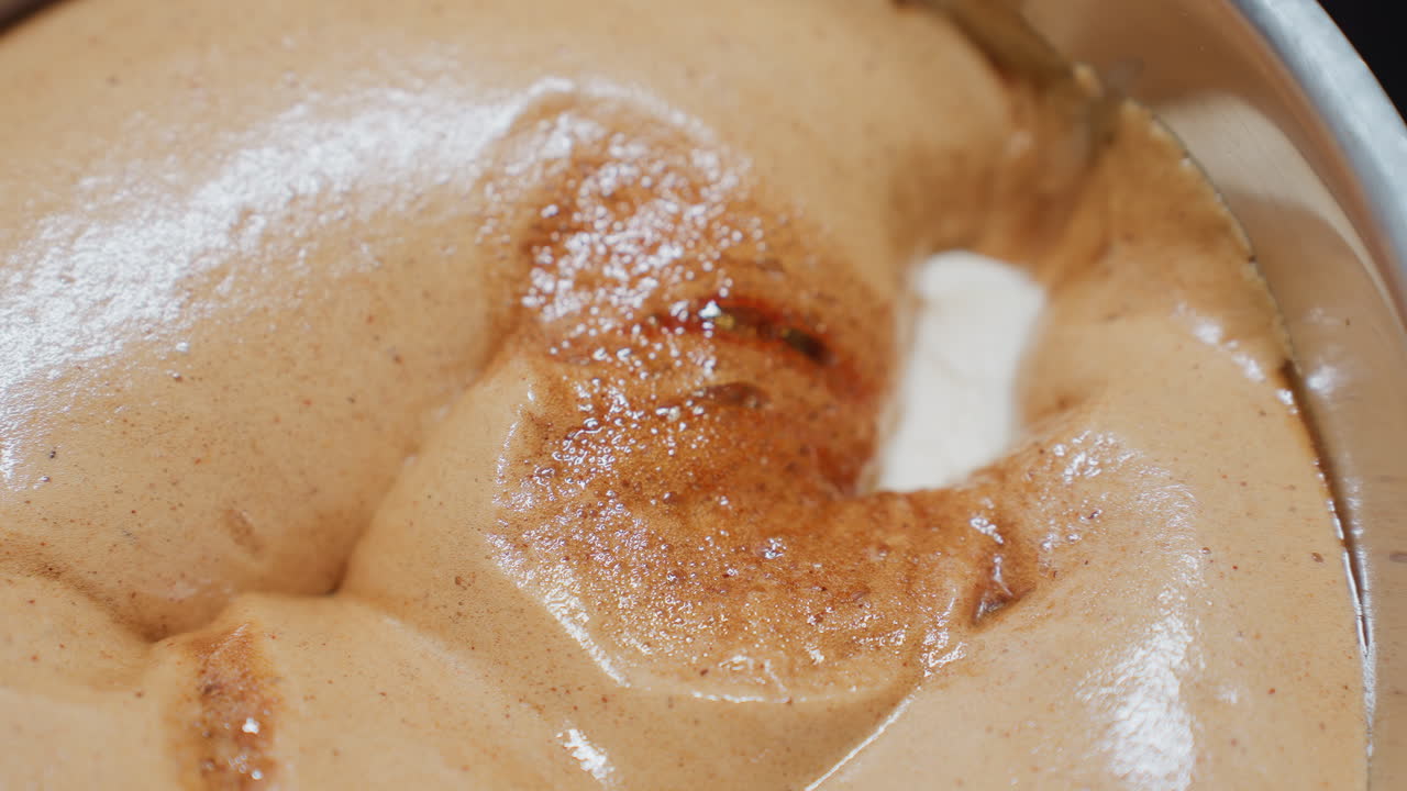 Close-up of creamy brown food with melting white butter inside a pot, the texture is smooth and glossy, with parts of the dish appearing aerated and bubbly