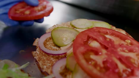 Tomato-slice-placed-on-burger-prepared-in-restaurant-kitchen,-close-up