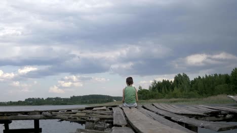 a lonely boy sits on the edge of the pier in windy rainy weather