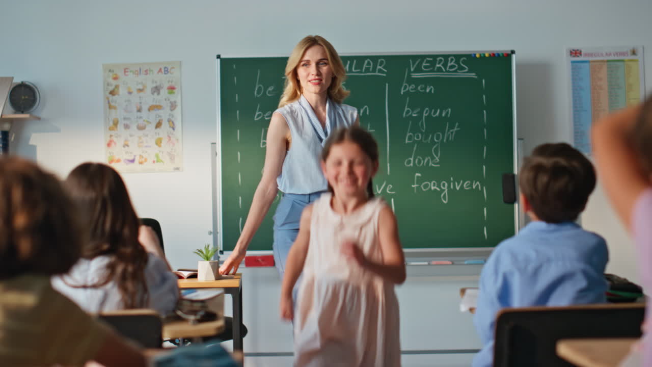 School girl speaking homework at class blackboard. Woman teacher listening