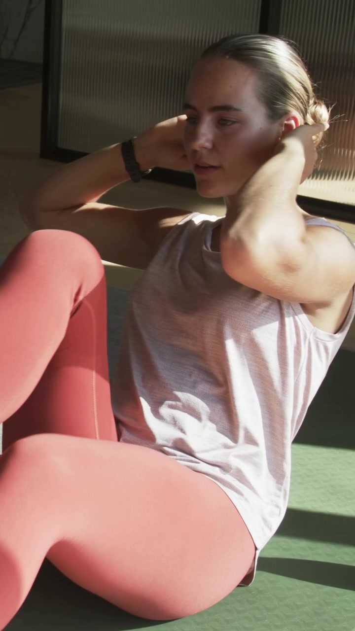 Video verticale: Donna in top rosa che fa crunch a bicicletta con le mani dietro la testa su un tappetino in palestra per allenare il core.