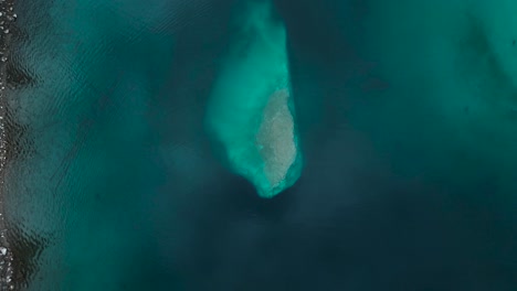 Top-down-view-of-a-rock-in-a-pristine-blue-water-lake-Caumasee-in-Switzerland