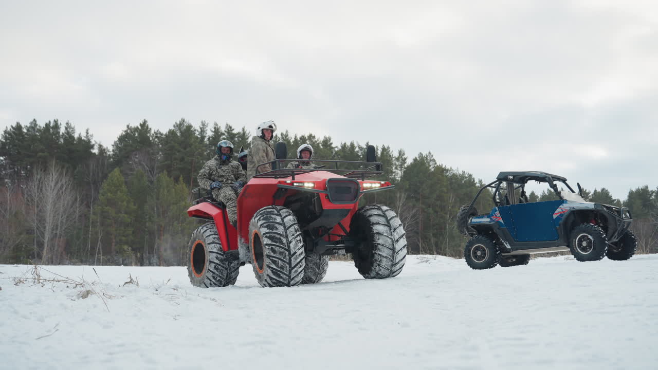 ATV rosso e UTV blu in un campo innevato con piloti caucasici che si preparano per un'estrema corsa invernale, con una pineta sullo sfondo, pneumatici da neve tassellati, caschi e giacche mimetiche, motori al minimo, luce fredda e nitida.