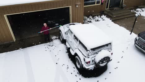 man brushing off his car after a late season snow flurry