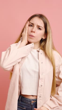 young woman suffering from headache on pink background