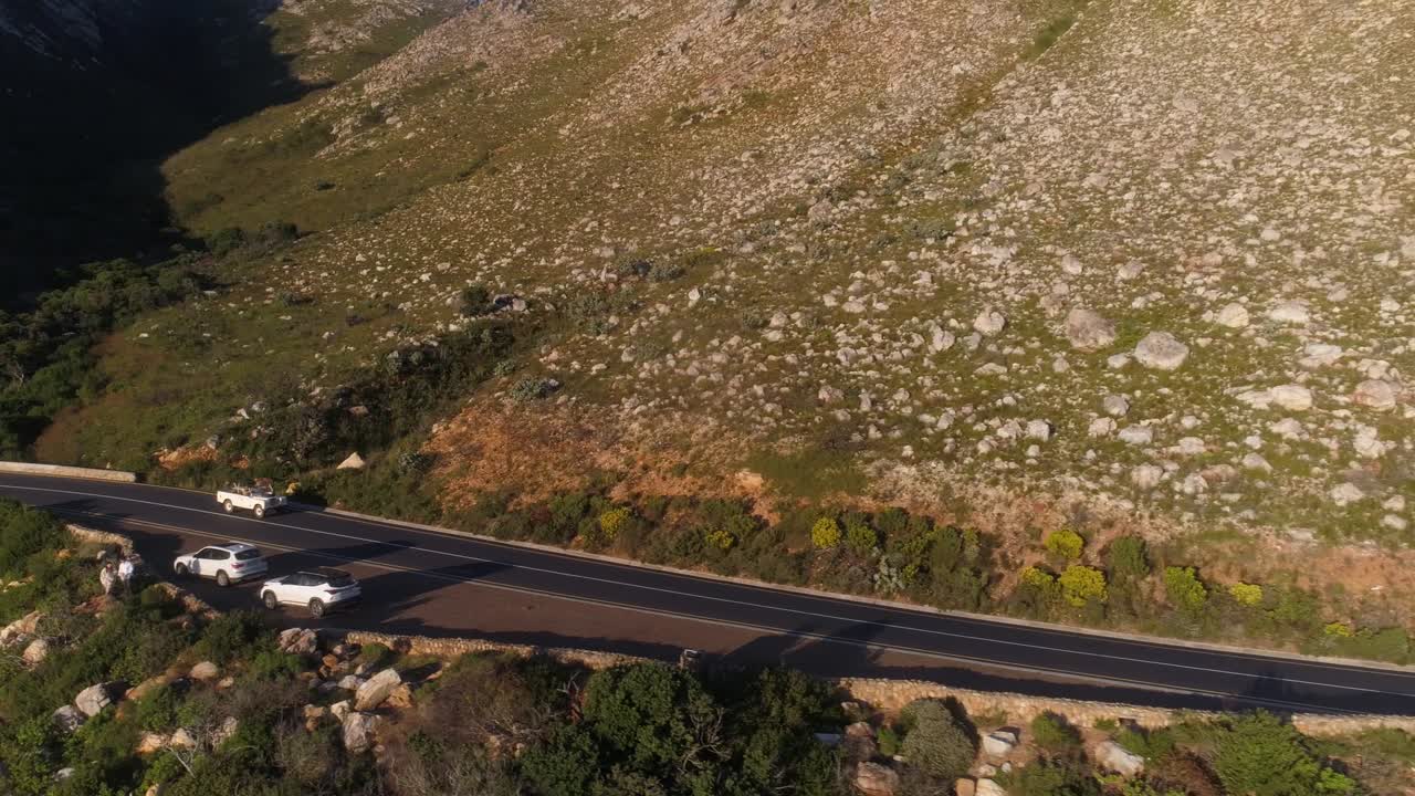 toma aérea de un dron de un land rover conduciendo por un paso de montaña hacia lo lejano mientras la vista se extiende hacia una vista del océano