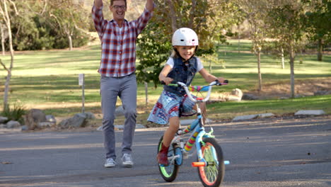padre enseñando a su hija a montar en bicicleta en un parque