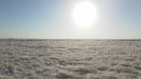 stationary ground level shot of the salt flats with a glaring sun hovering over the horizon