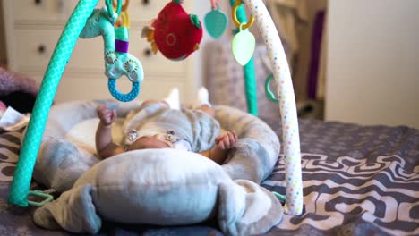charming new born baby girl moves her legs and hands in cradle while staring at colorful toys above her