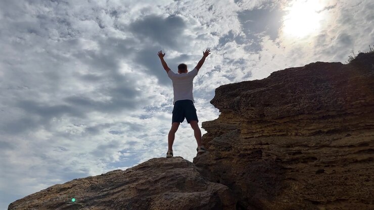 Man Standing on Rocky Cliff Edge Raising Arms to Sky