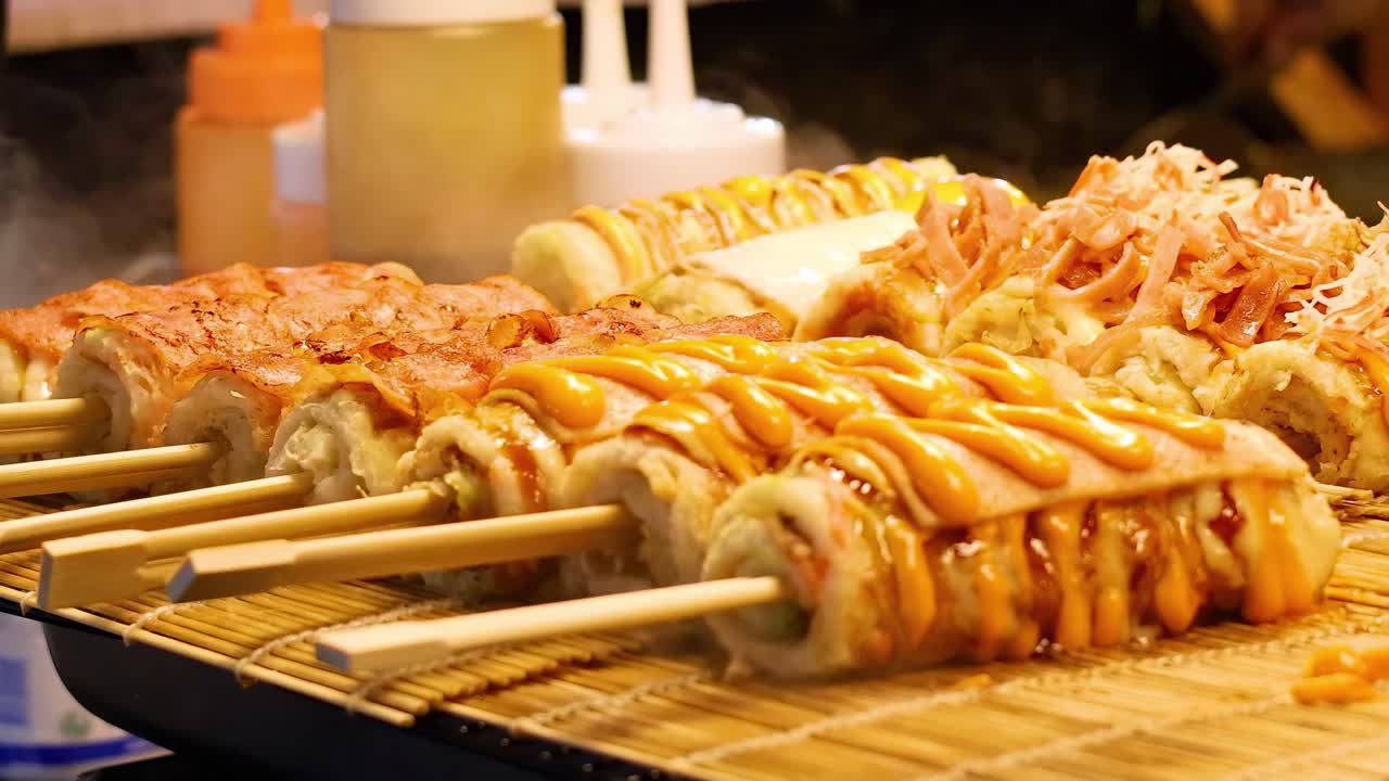 Close-up of skewered food with drizzled sauces, ready to serve at a bustling night market.