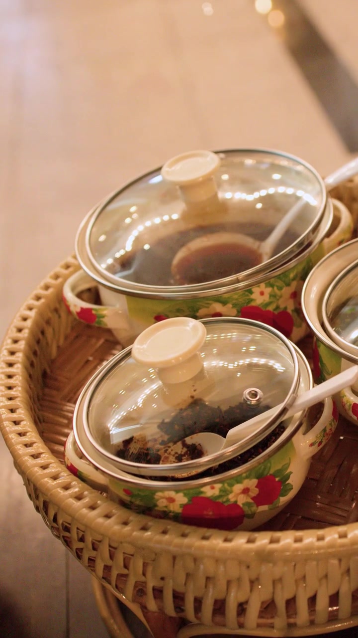 Close-up shot of traditional Burmese dishes in floral enamel pots on a wicker tray.