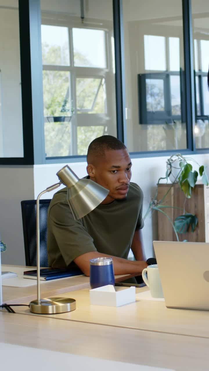 Vertical video: Turning worker in olive tee responding to peer coming about work at office laptop
