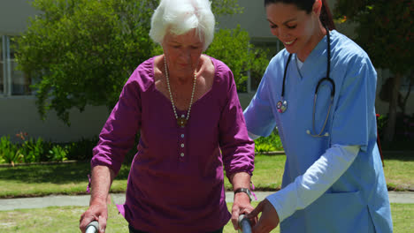 front view of caucasian female doctor helping senior patient to walk with walker in the garden of nu