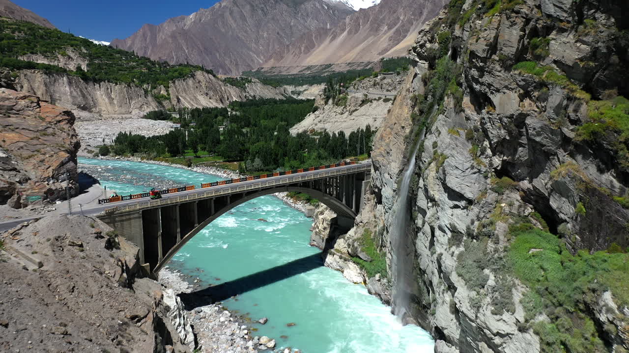 tiro de dron del río de agua azul turquesa que fluye bajo un puente en la cordillera de karakoram a lo largo de la carretera de karakoram, moviéndose hacia el puente con tráfico