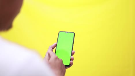 close up studio shot of head and hand of afro american man holding his smartphone with green screen and looking on it, shifting, touching screen