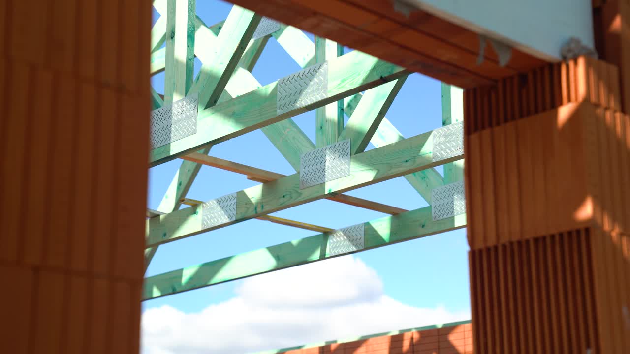 View through unfinished brick wall window frame of house showing timber roof trusses above