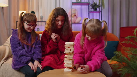 three siblings children girls playing with blocks board game, build tower from wooden bricks at home