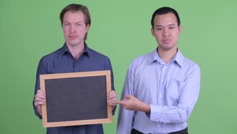 two businessman showing bad news from blackboard against green studio background