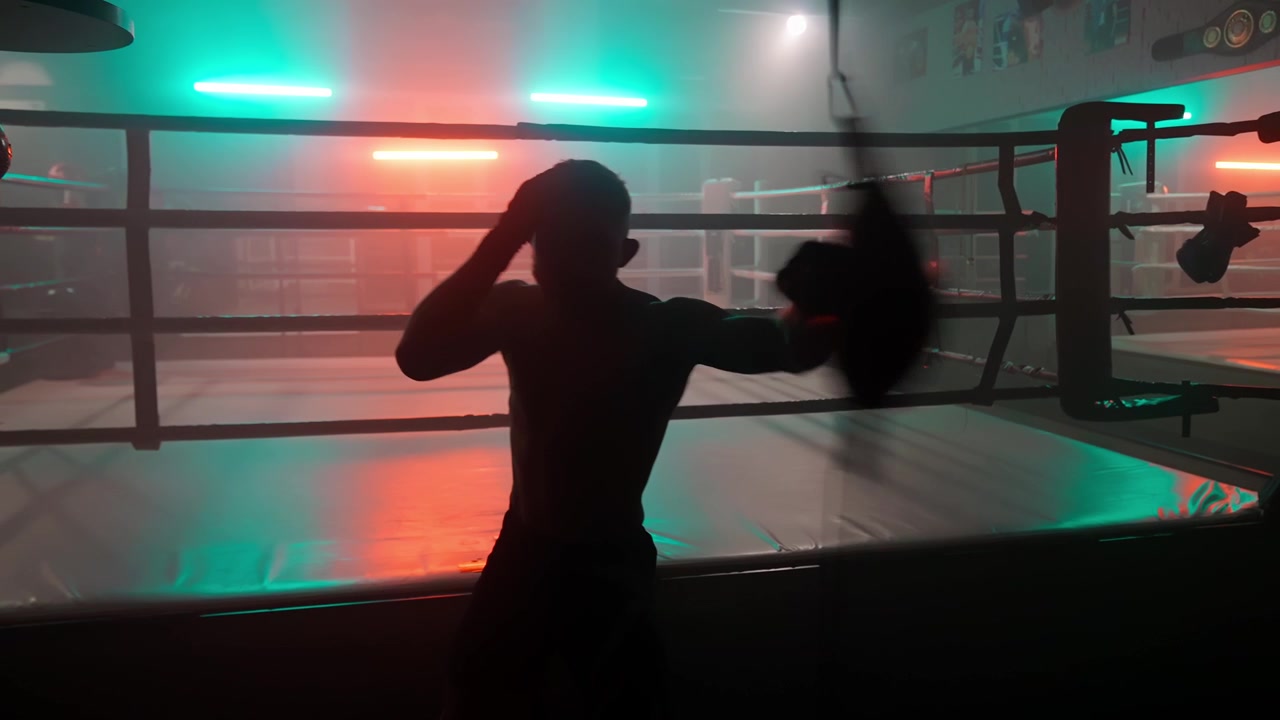 Silhuet af en bokser, der træner med en speedbag i et mørkt fitnesscenter