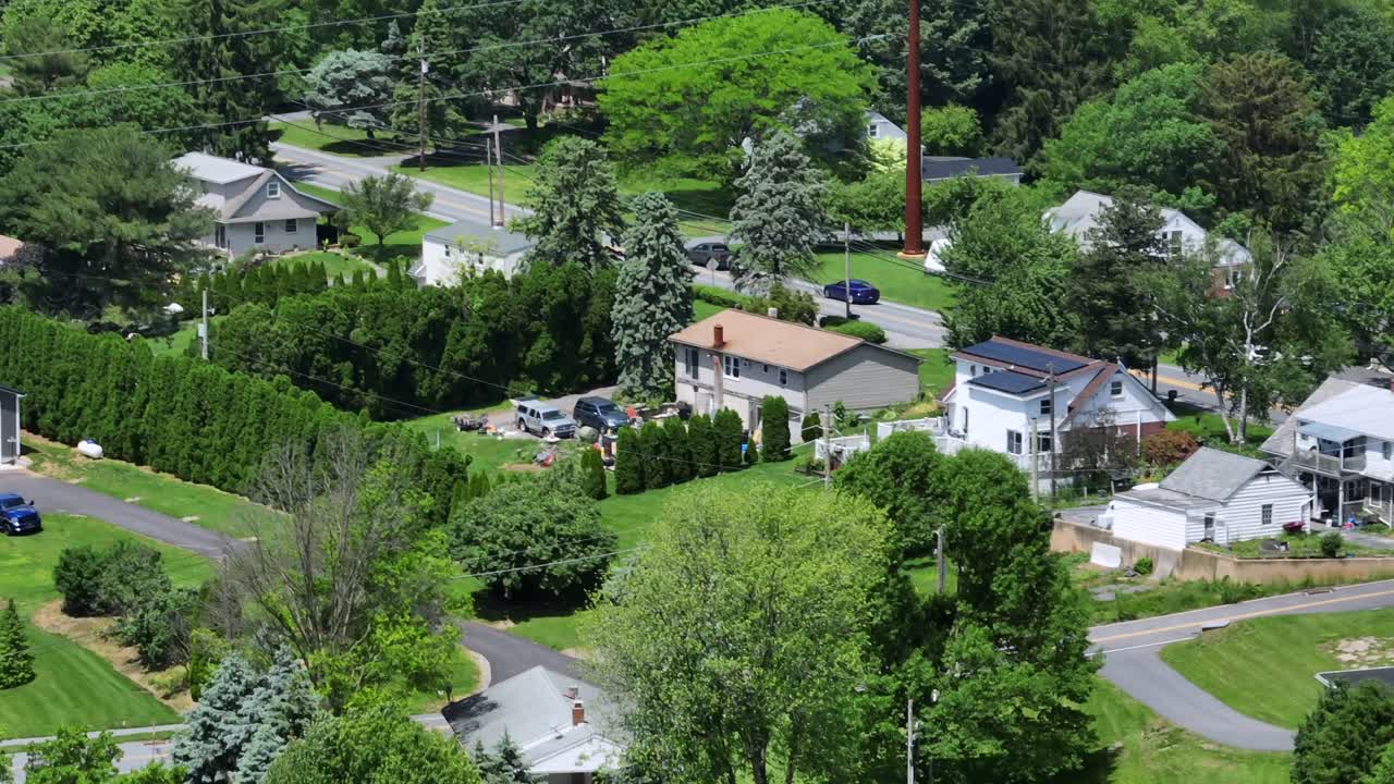 Driving cars on suburb road between houses and green trees. Sunny day in spring. Aerial tilt up wide shot. American city with homes in suburb. Forest trees in distance.