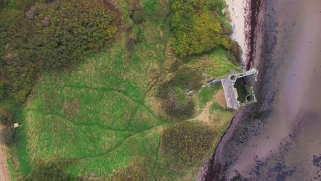 Aerial-top-down-rising-over-ruins-of-ancient-Scottish-castle-on-headland-overlooking-lake