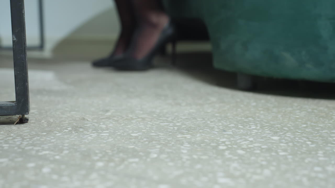 Close up of woman leg in black stiletto heel as she walks across tiled office floor toward seat, showcasing elegant professional style and poised movement in workplace environment