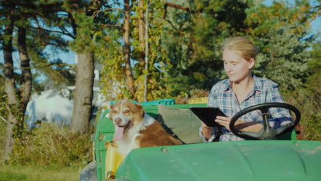 a female farmer on a small tractor rides along her farm beside her her dog