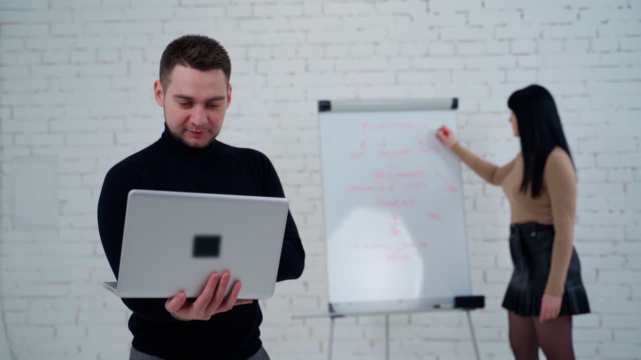 Couple working together. Businesswoman looking at marker board while male employee standing with laptop