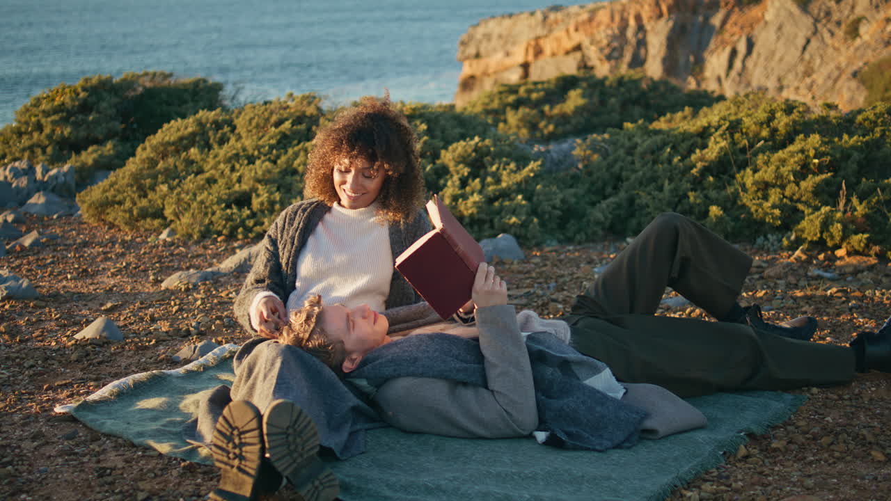 Famiglia tranquilla che legge un libro nella natura, trascorrendo il fine settimana. Uomo sdraiato sulle ginocchia della donna.