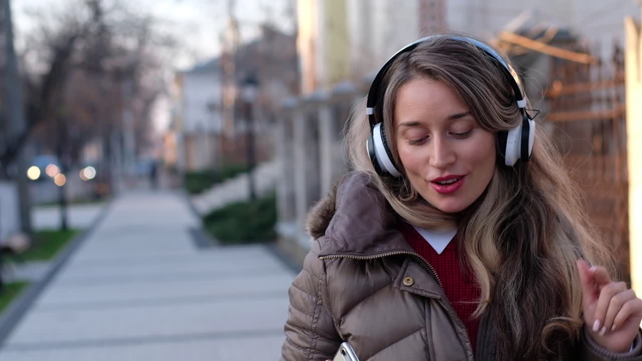 Woman listening to music in her headphones while singing along and dancing in the street