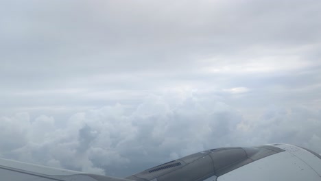 an aerial view from an airplane window reveals the aircraft wing and engine, framed against a dramatic expanse of dense, textured clouds