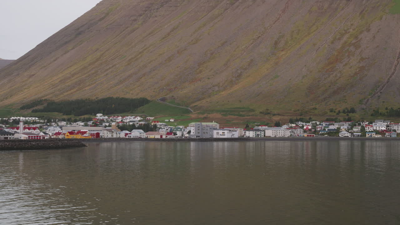 POV von einem Schiff, das an einem bewölkten Tag in den Hafen von Isafjördur, Island, einfährt, eine kleine isländische Stadt