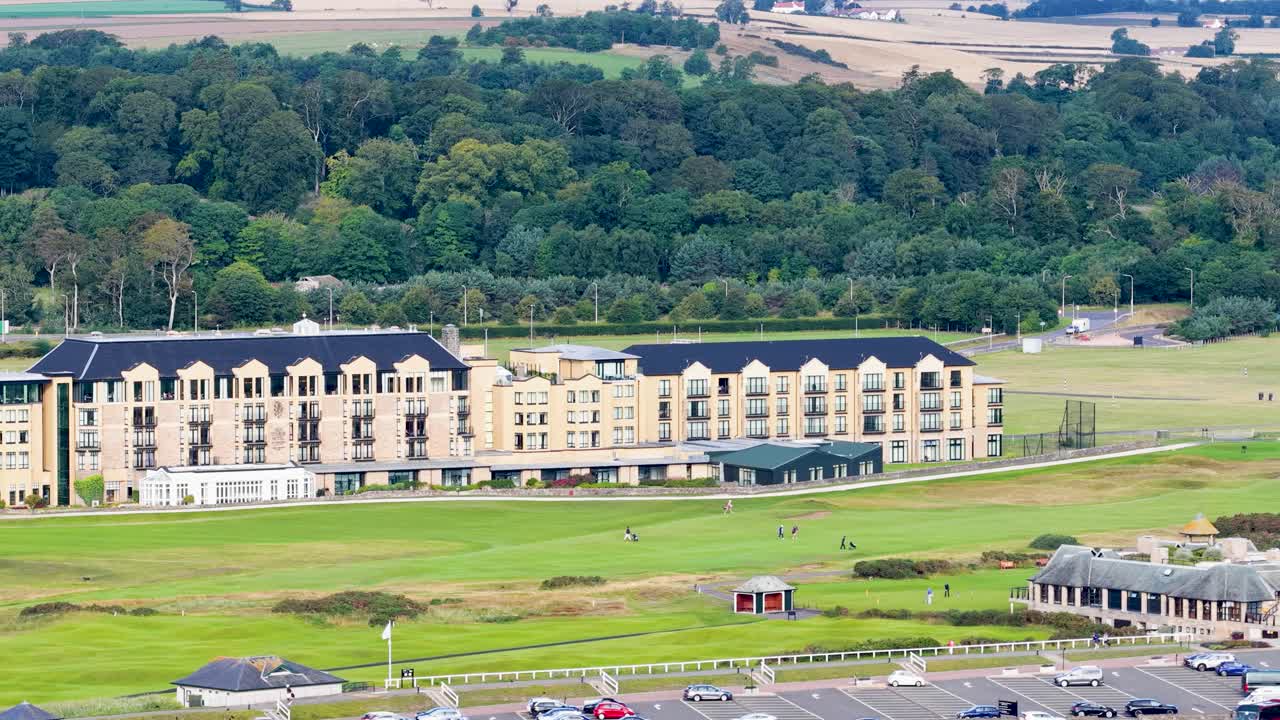 Wide aerial pan over luxury hotel, golf course, fairway, and green hills in daylight