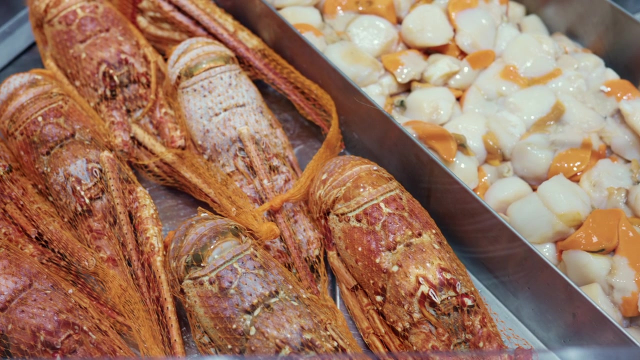 Fresh spiny lobsters in nets alongside a crab on a metal tray, ready for sale at a fish market stall