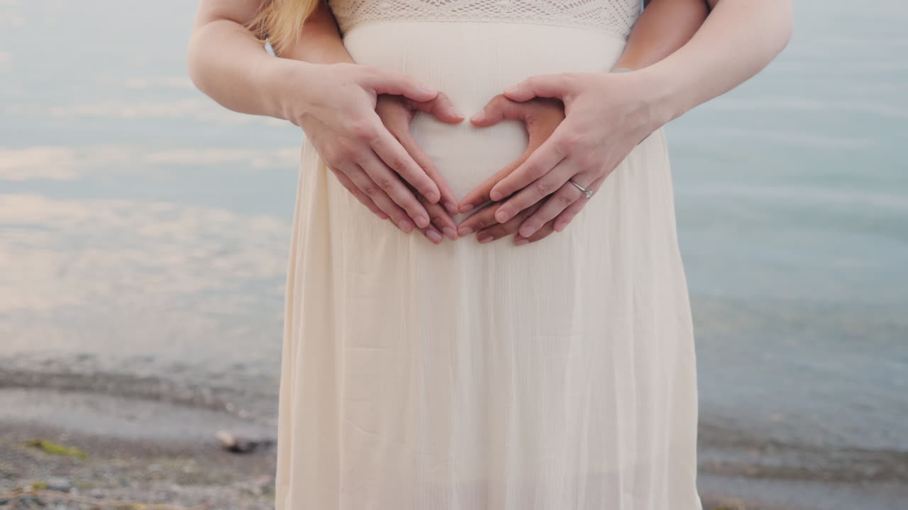 젊은 부부는 임신한 여자의 배에 마음을 보여줍니다