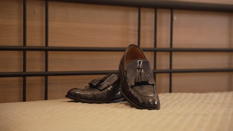 stylish black leather tassel loafers placed on a bed with a wooden headboard