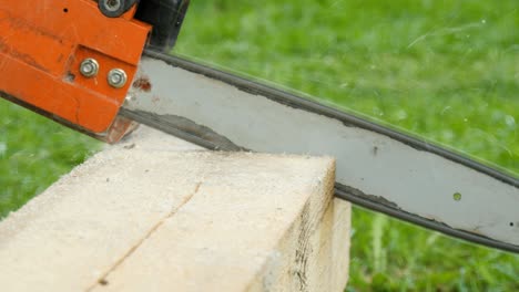 A worker cuts a wooden beam with a gasoline saw close-up