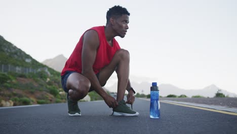 African-american-man-tying-his-shoe-laces-on-the-road