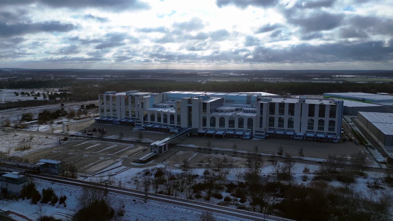 Large distribution center like an industrial castle with loading docks and parking lot under a cloudy sky in winter. Majestic aerial view flight ascending drone