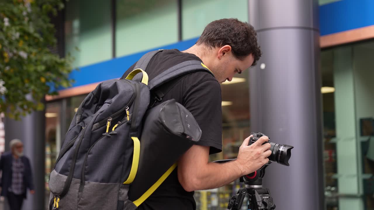 Young caucasian man is holding and adjusting his camera that is on a tripod