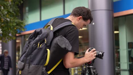 Young-caucasian-man-is-holding-and-adjusting-his-camera-that-is-on-a-tripod